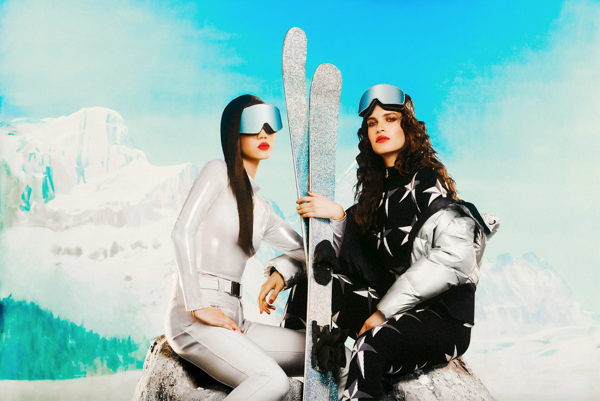 Two models wearing alt*ego ski goggles embellished with Swarovski crystals, posing with sparkling skis.
